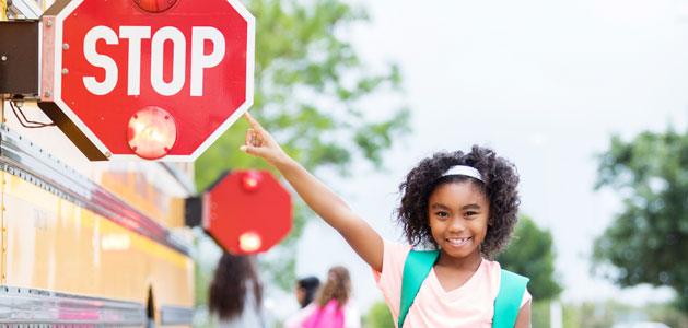 image of girl pointing to the stop sign on the side of a school bus